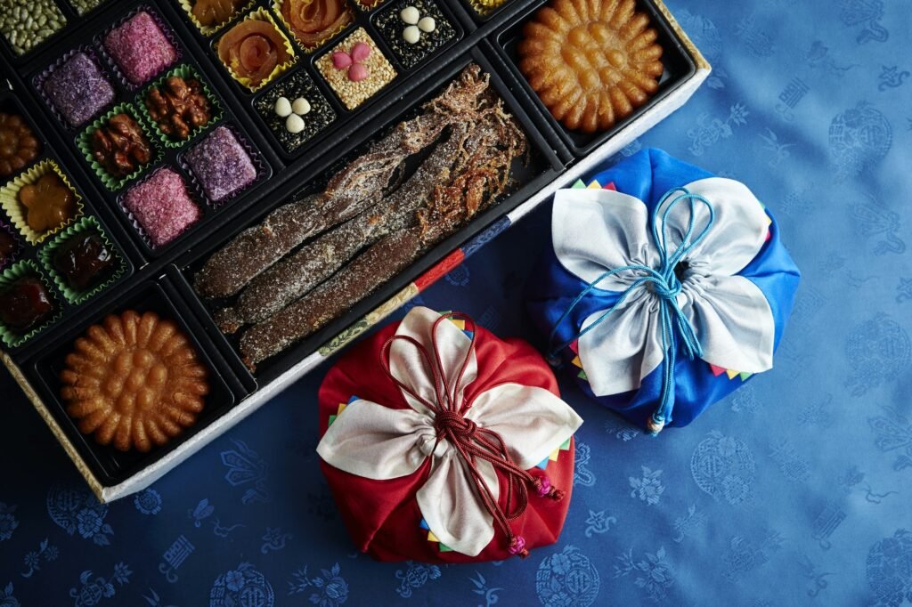 Top view of a box full of Korean sweets, surrounded by colorfully wrapped gifts